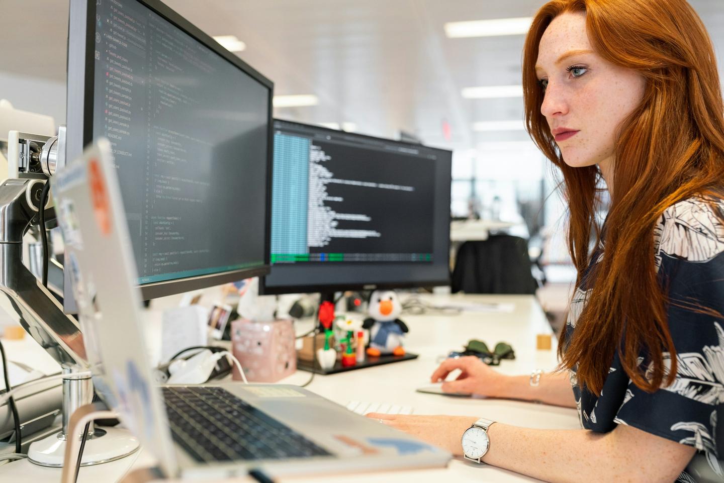 Software developer working with code on two monitors in a bright office