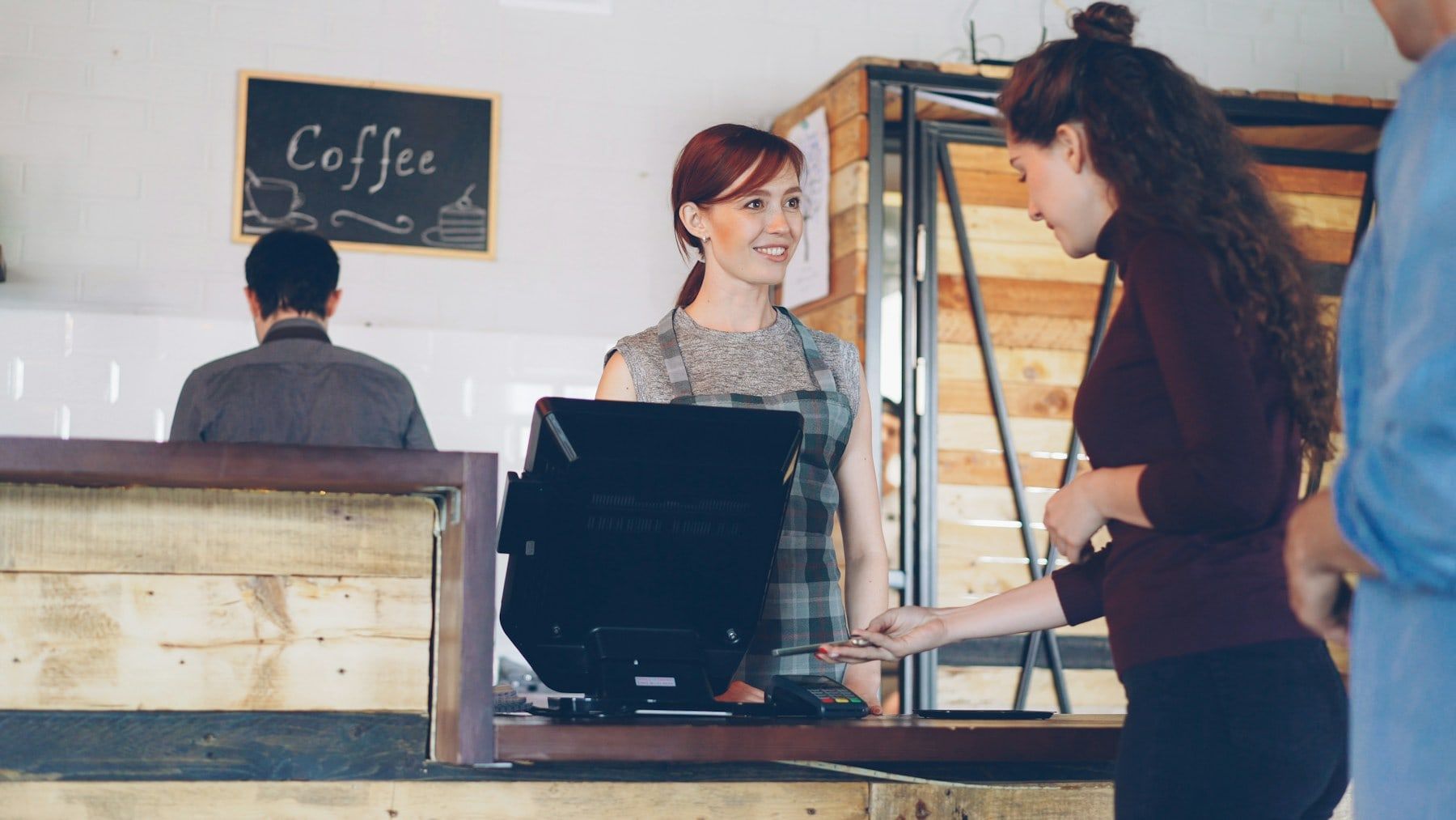 Customer paying at a touch-screen POS terminal on a café counter